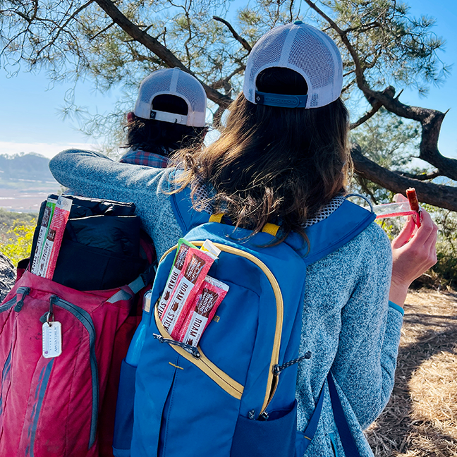 Two people taking a break from hiking to eat a Singing Pastures Roam Stick