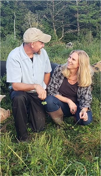 John & Holly Arbuckle in a field with pasture raised pigs