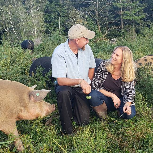John & Holly Arbuckcle in a field with pigs surrounding